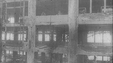  Schwarz-weiß Aufnahme von einem zerstörten mehrstöckigen Haus.