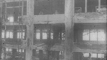  Schwarz-weiß Aufnahme von einem zerstörten mehrstöckigen Haus.