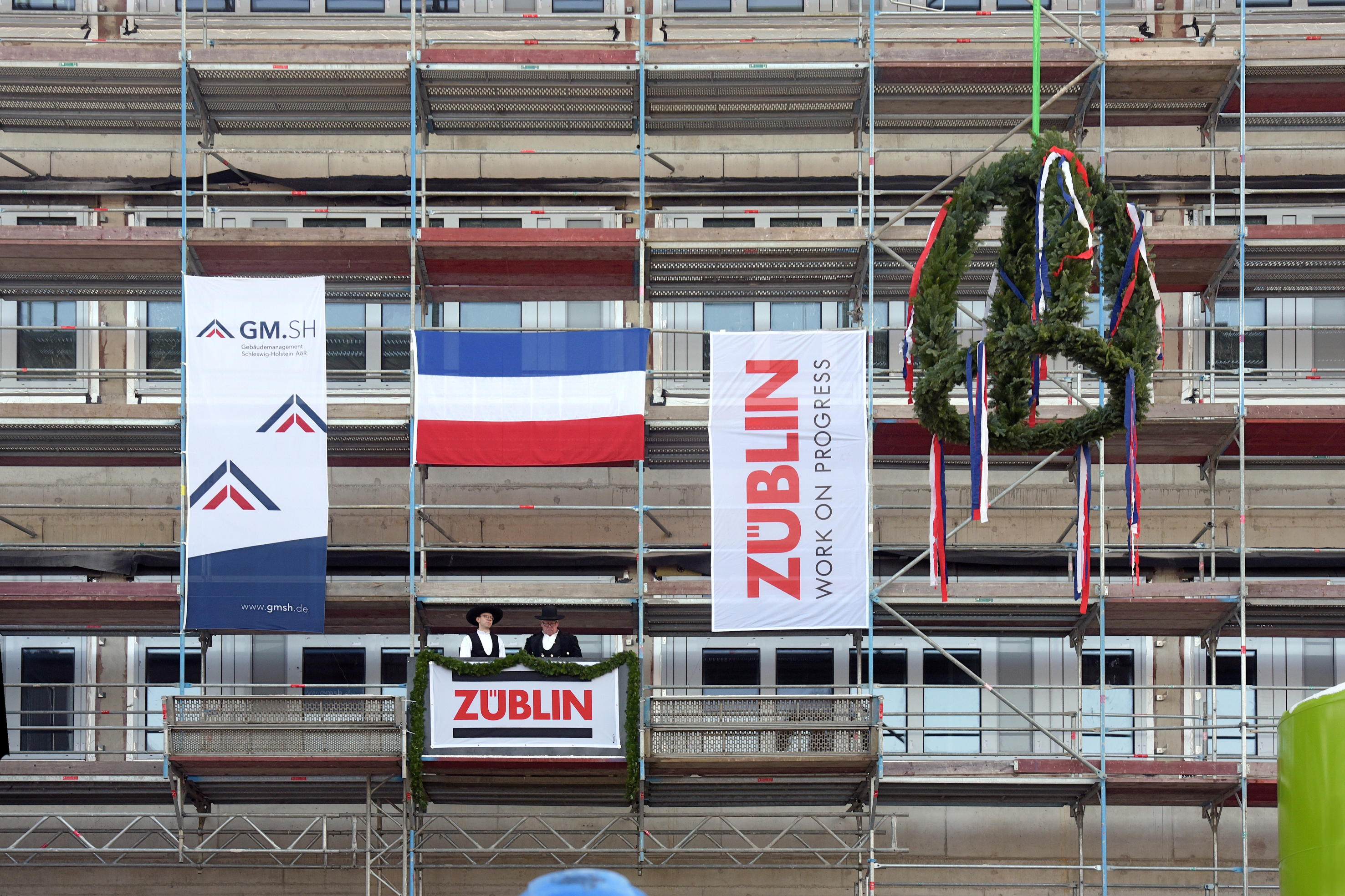 Foto von zwei Personen, die auf einem Gerüst stehen und den Richtspruch verkünden. 