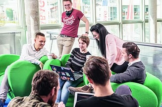 Das Bild zeigt eine Gruppe von jungen Personen auf grünen Stoffsesseln, im Hintergrund Glaswände