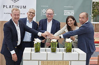 Foto von mehreren Personen, die ihre auf eine Röhre legen zur Grundsteinlegung.   