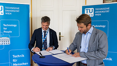 Photo of two people at a bar table signing documents