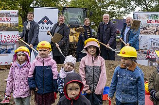 Foto vom symbolischen Spartenstich. Im Hintergrund sind mehrere Personen im Anzug zusehen. Im Vordergrund stehen Kinder, die einen Helm anhaben. 