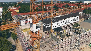 Foto von einem Kran auf einer Baustelle der ein Banner trägt.  