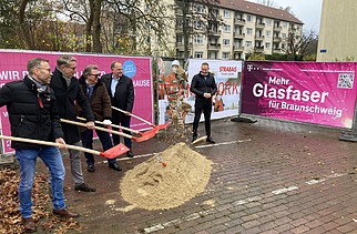 Foto von mehreren Personen beim symbolischen Spatenstich mit Schaufeln in der Hand, dahinter Bautransparente mit der Aufschrift Glasfaser