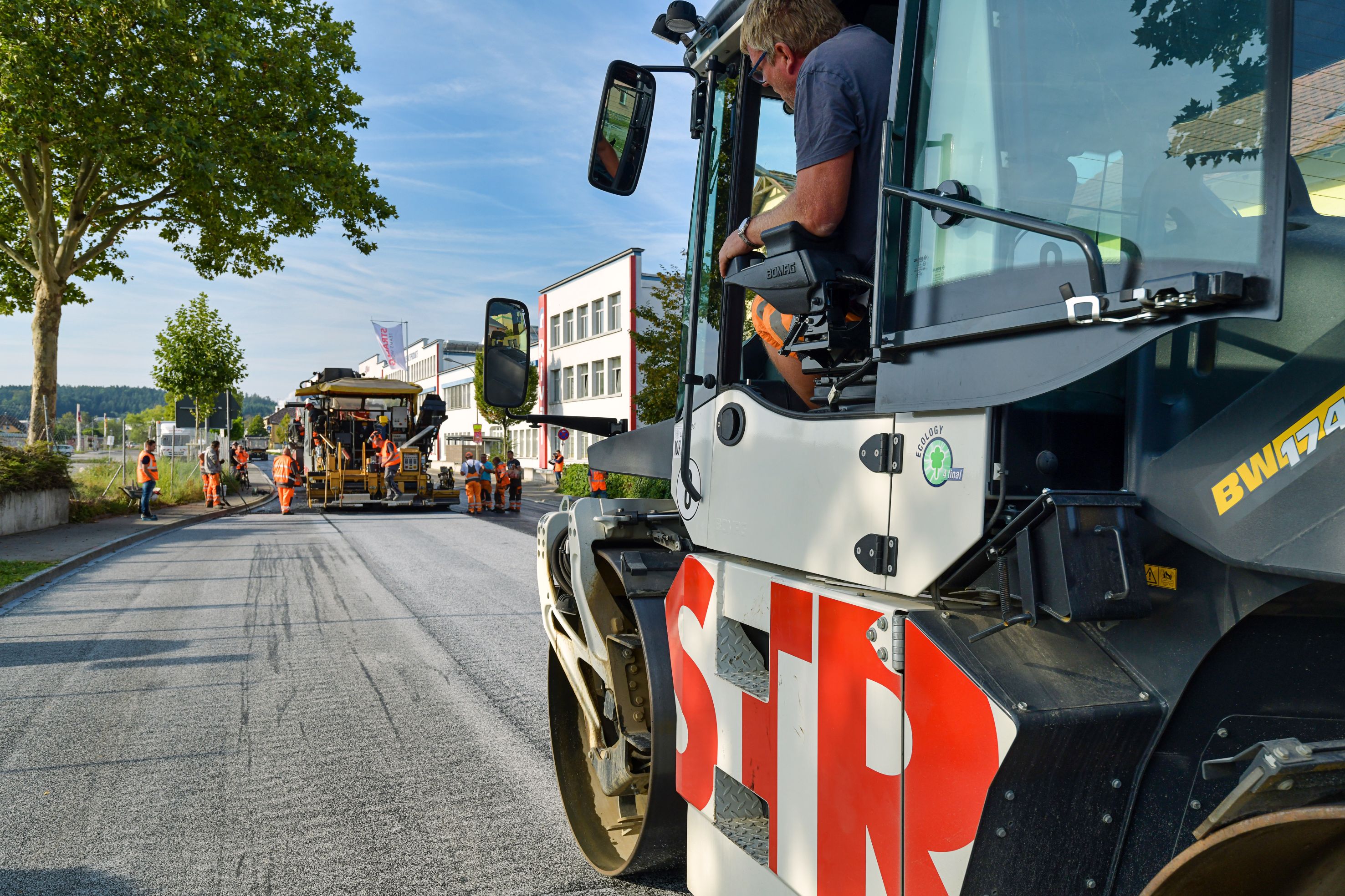 Foto einer Straßenbauschine von der Seite, im Hintergrund eine weitere Maschine