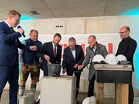 Foto von mehreren Männern im Anzug, die Beton in einen Stein verstreichen. 