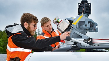 Foto von zwei Personen in Schutzwesten mit einem mobilen Laserscanner