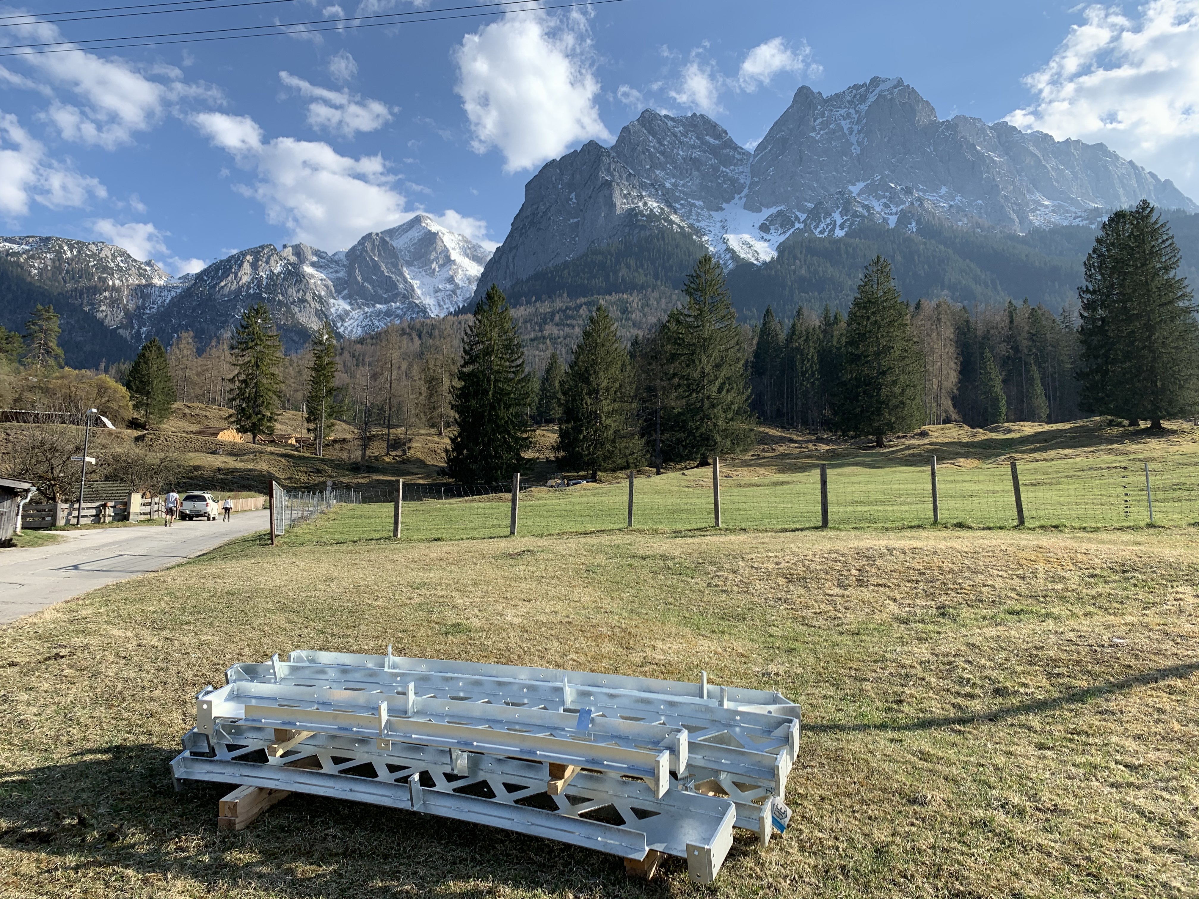 Foto von Stahlelementen die auf einer Wise vor einem Gebirge liegen.   