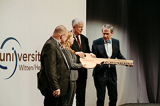Foto von vier Personen die den Schlüssel zur Universität halten.  