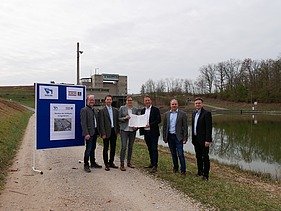 Photo of five people standing on a gravel road, to the left a blue sign