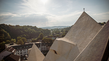  Foto von einer Kirche in einer Stadt, mit Blick von den Dächern der Kirsche. Drumherum ist ein Wald.