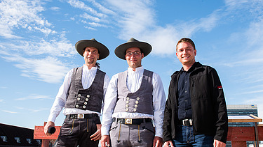 Foto von drei freundlich schauenden Männern beim hissen des Richtkranzkranz.