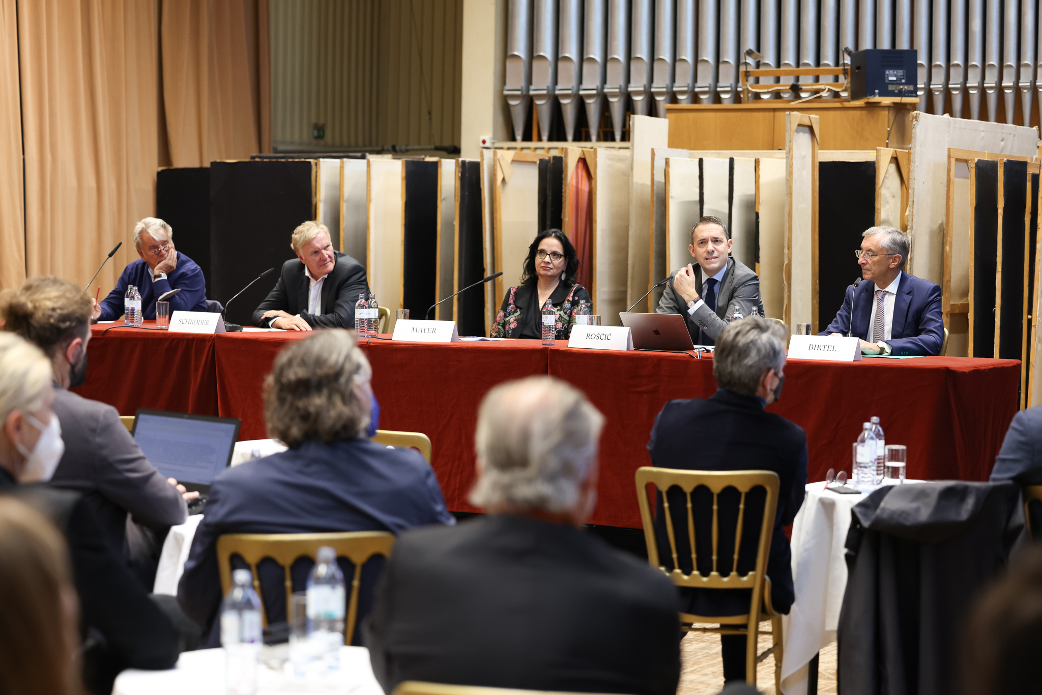 Foto einer Pressekonferenz, auf einer Bühne sitzen für Personen, die vor Publikaum vortragen