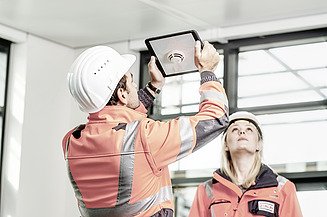 Zu sehen sind zwei Mitarbeiter:innen der STRABAG, die mit einem Tablet ein Objekt an der Deckenwand begutachten.