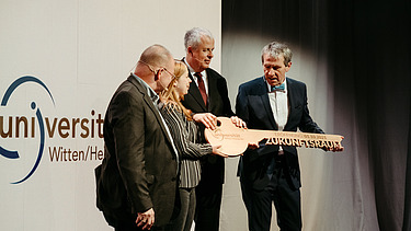 Foto von vier Personen die den Schlüssel zur Universität halten.  