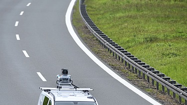 Foto eines Fahrzeuges mit einem Vermessungsgerät auf dem Dach auf einer zweispurigen Fahrbahn