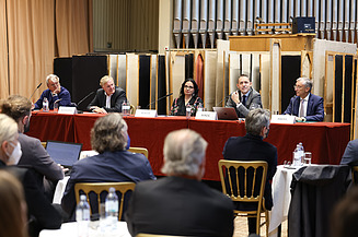 Foto einer Pressekonferenz, auf einer Bühne sitzen für Personen, die vor Publikaum vortragen