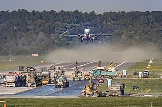 Foto einer Baustelle auf einer Flugpiste, dahinter startet gerade ein Flugzeug