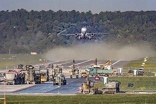 Foto einer Baustelle auf einer Flugpiste, dahinter startet gerade ein Flugzeug