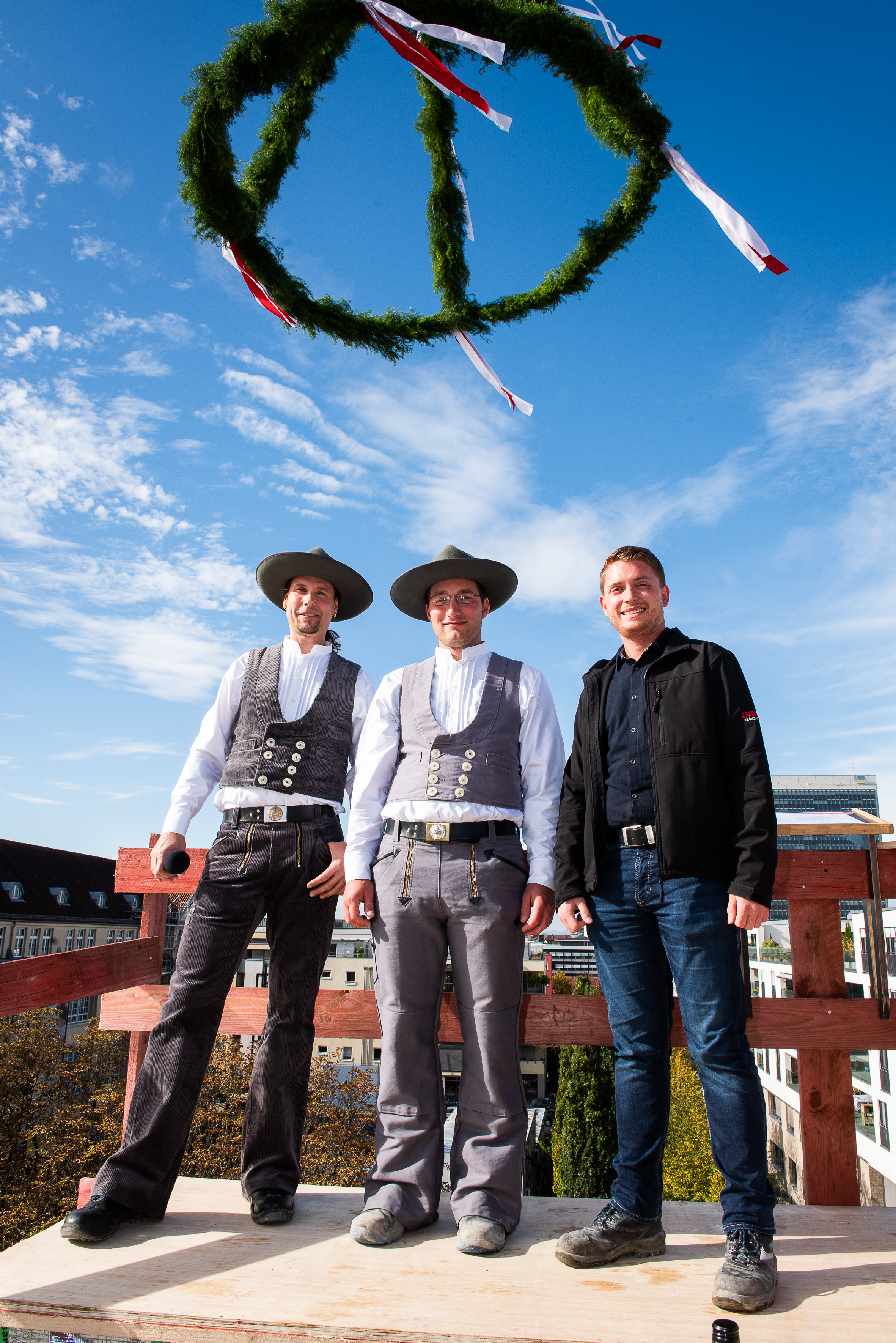 Foto von drei freundlich schauenden Männern beim hissen des Richtkranzkranz.
