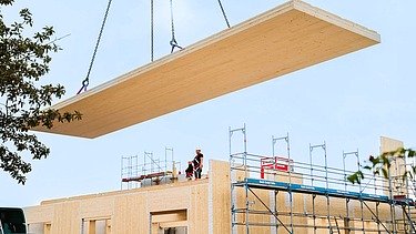 Foto von Neubau am Campus Witten/Herdecke. Ein Kran trägt eine Holzplatte. 