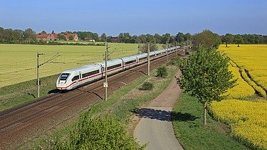 Foto einer Bahnstrecke mit einem weißen Schnellzug, links und rechts blühende, gelbe Rapsfelder