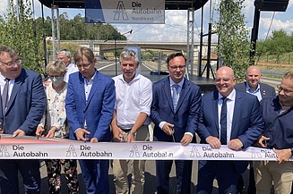 Foto von der feierlichen Verkehrsfreigabe, mehrere Personen durchschneiden ein dickes Band