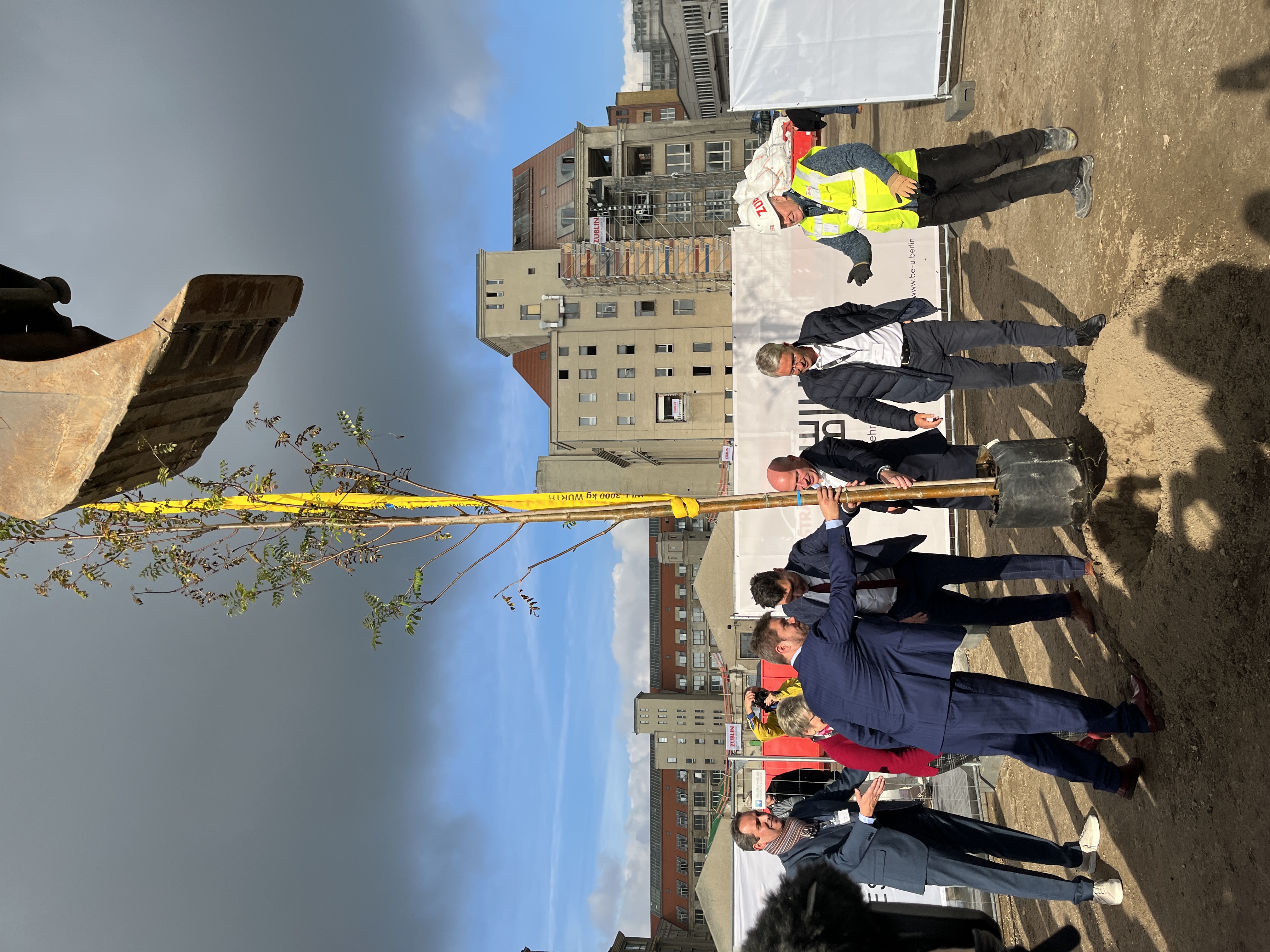 Foto von mehreren Personen im Anzug die einen Baum einpflanzen.   