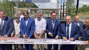 Foto von der feierlichen Verkehrsfreigabe, mehrere Personen durchschneiden ein dickes Band