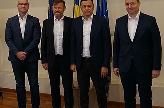 Photo of four people standing in front of three flags