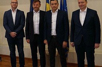 Foto von vier stehenden Personen vor drei Flaggen