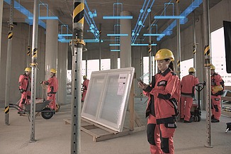 Foto von einer Baustelle in einem Gebäude. Es sind mehrere Personen mit Schutzausrüstung zusehen. Die Decke wird von Stangen getragen.   