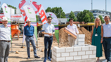 Foto von mehren Personen, die eine symbolische Grundsteinlegung durchführen. 