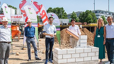 Foto von mehren Personen, die eine symbolische Grundsteinlegung durchführen. 