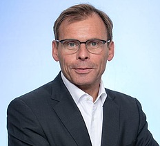 Portrait von einem Mann im Anzug mit Brille. 