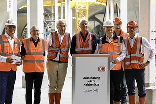 Foto von mehreren Personen in Schutzausrüstung die vor einem Rednerpult stehen. 