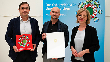 Foto von drei Personen, die beiden links halten jeweils eine Urkunde in den Händen