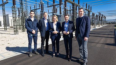 Foto von fünf Personen, die vor einem Umspannwerk stehen