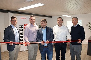 Foto von fünf Männern die ein rotes Band in einem Büroroaum durchschneiden