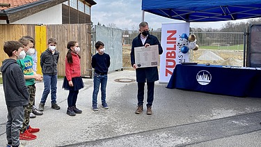 Foto von Kindern und einem Mann, die an einer Zeitkapsel-Zeremonie teilnehmen. 