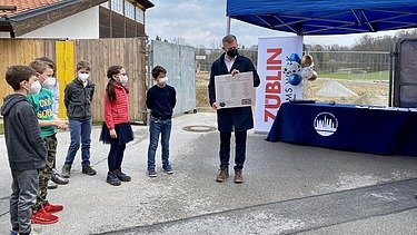 Foto von Kindern und einem Mann, die an einer Zeitkapsel-Zeremonie teilnehmen. 