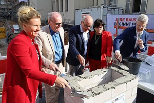 Photo of several people, smartly dressed, spreading concrete on a masonry wall.