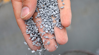 Foto einer Hand, die graue Kügelchen runter rieseln lässt