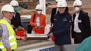 Foto von der Grundsteinlegung im Klinikum, mehrere Personen halten eine Zeitkapsel. 