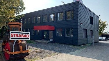 Foto eines schwarzen, einstöckigen Gebäudes, im Vordergrund eine STRABAG Bautafel