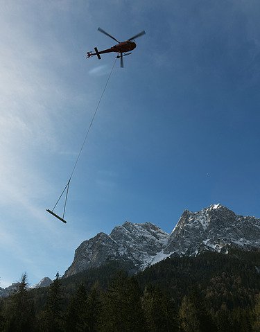 Foto von einem Hubschrauber der Material an einem Seil transportier in einem Gebirge.  