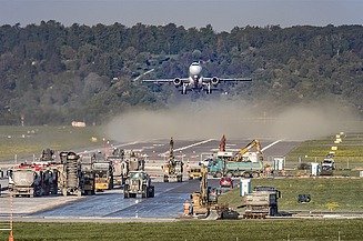 Foto einer Baustelle auf einer Flugpiste, dahinter startet gerade ein Flugzeug
