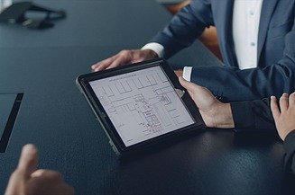 Foto von einem einer Besprechung mit einem Fokus auf ein I-Pad. Auf dem I-Pad ist ein Bauplan zusehen.  