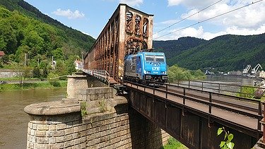 Foto von einer Eisenbahnbrücke aus rostigem Stahl mit einem blauen Zug